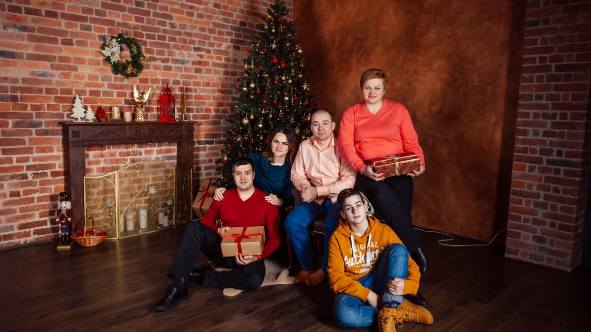 A family posing with Christmas gifts by a decorated tree indoors, exuding holiday warmth.