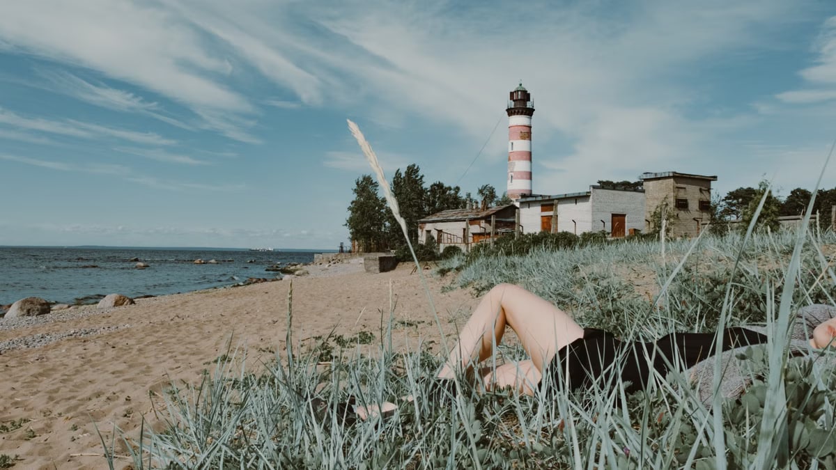 A person relaxes on a beach near a historic lighthouse, surrounded by nature.